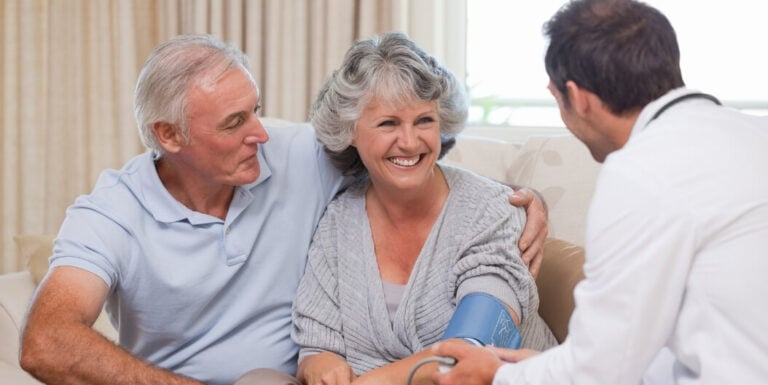 Male Doctor Checking Blood Pressure for Elderly Couple at Memory Care Facility